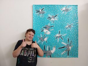 Artist Ebony Stevens standing next to a large painting that features several seagulls on a blue dotted background.